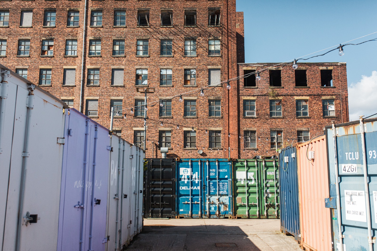 A collection of brightly coloured shipping containers in the shadow of an old mill